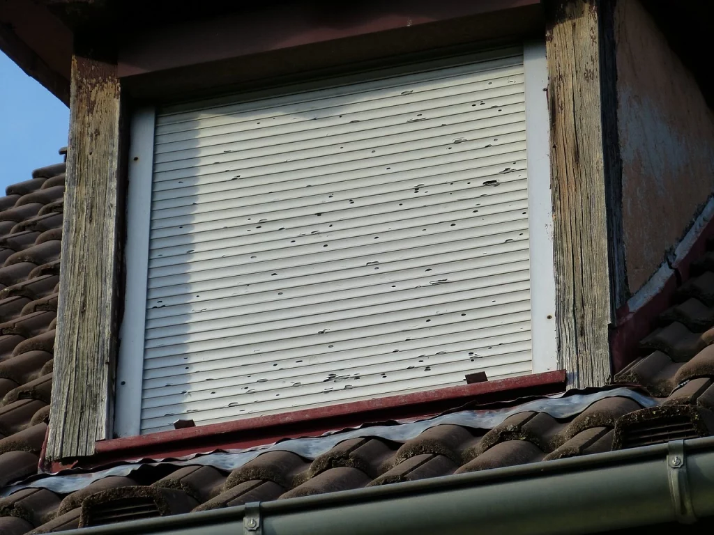 Das Bild zeigt eine verwitterte Dachgaube mit einem defekten Rollo